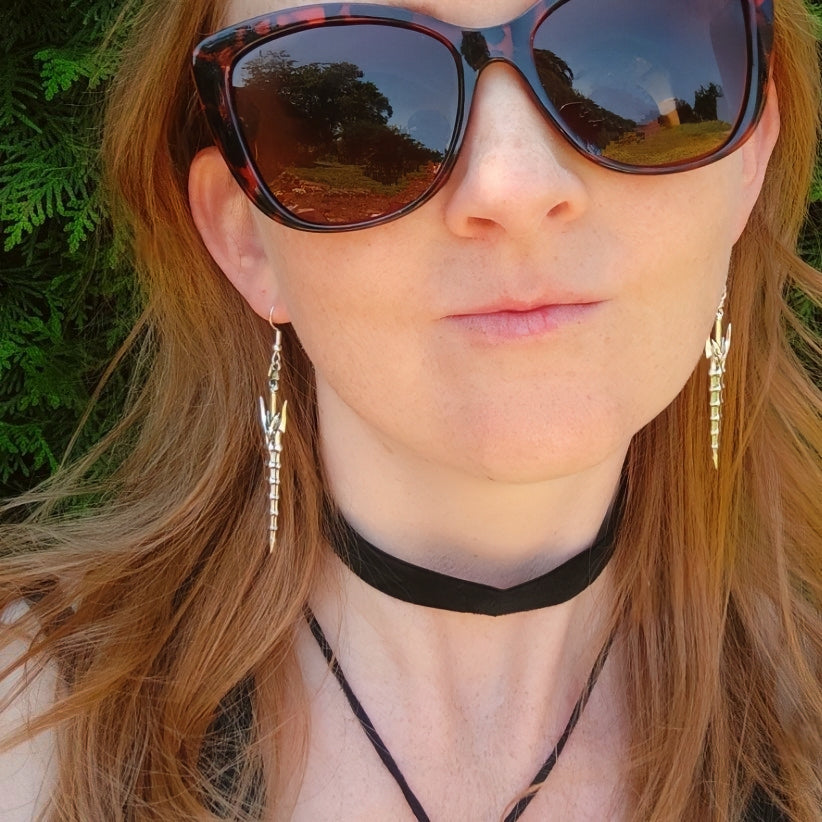 A woman wearing silver sword earrings with green background