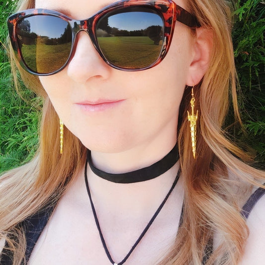 Woman wearing gold fantasy sword earrings with a blurred natural background