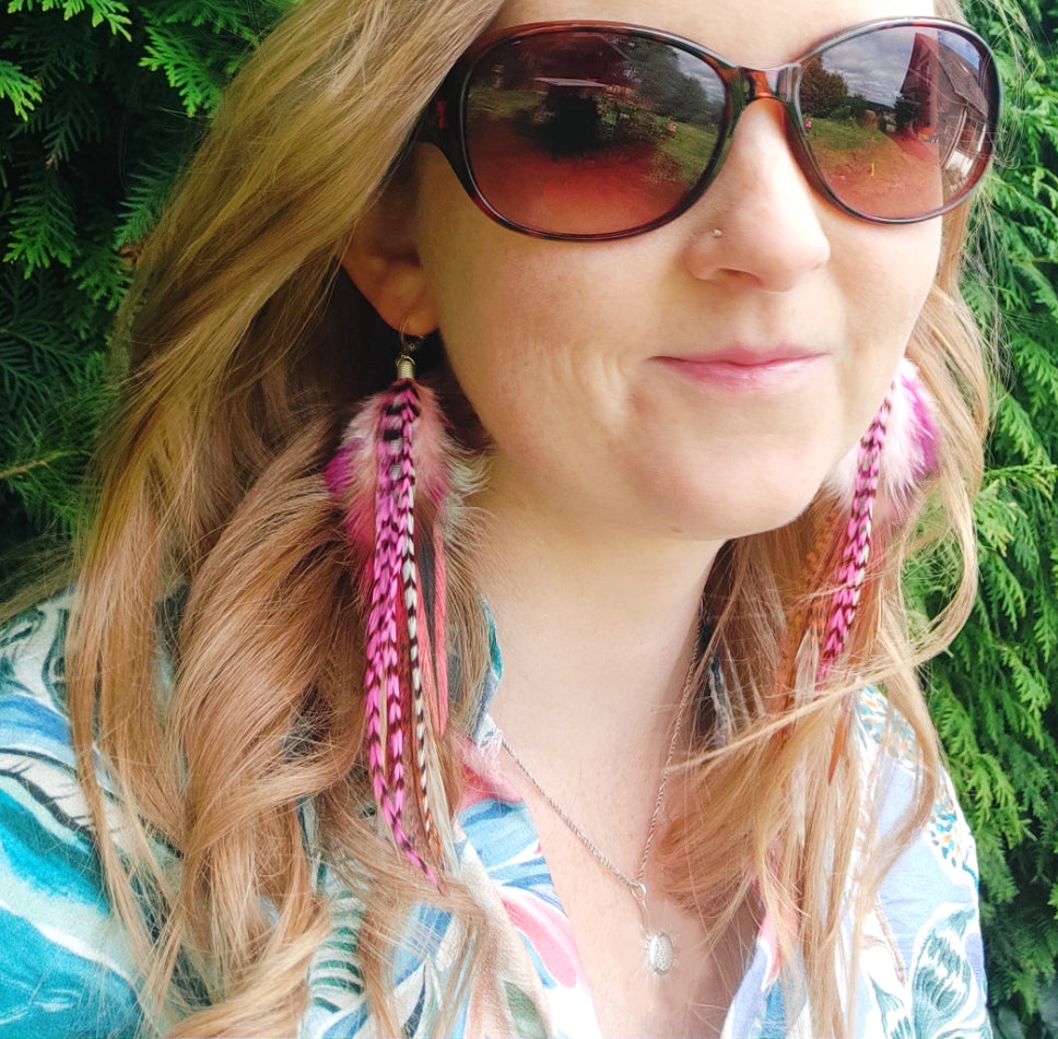 Woman wearing long pink feather earrings and sunglasses with a green natural background