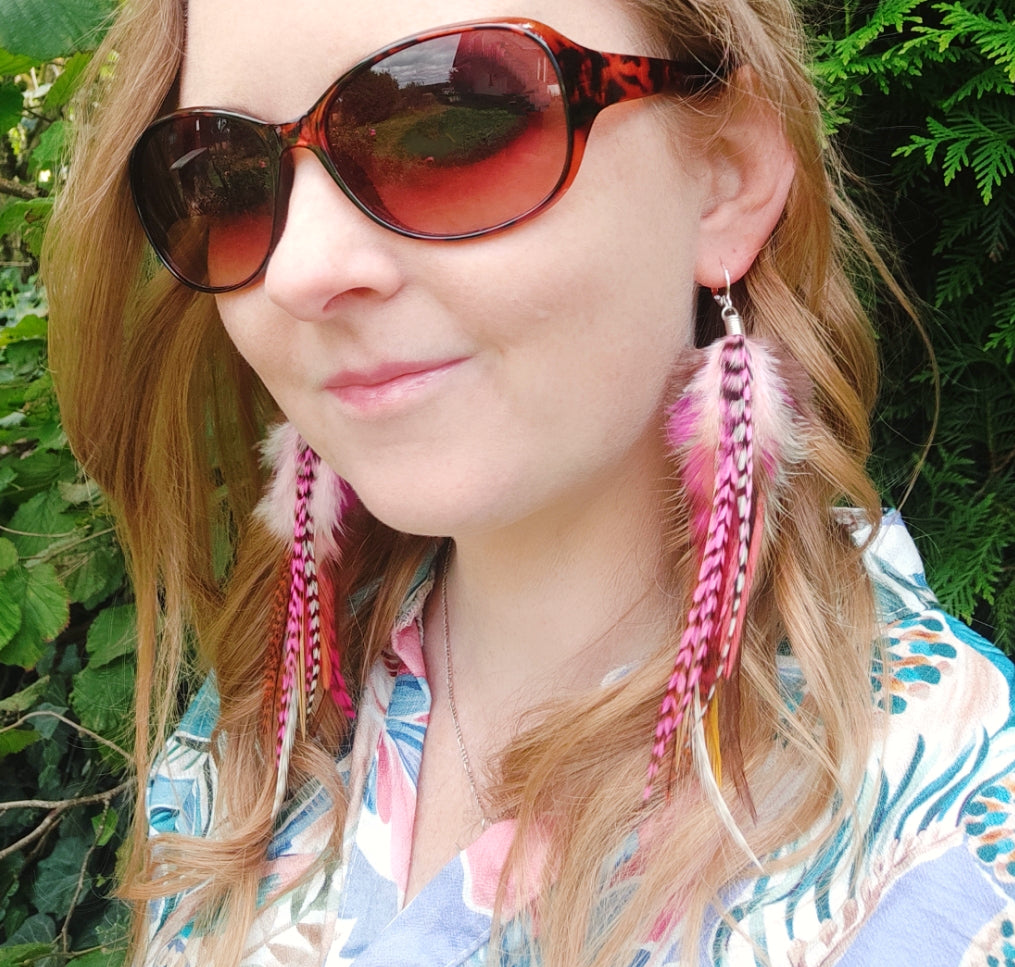 Woman wearing sunglasses and long feather earrings with a green background. Boho hippie style