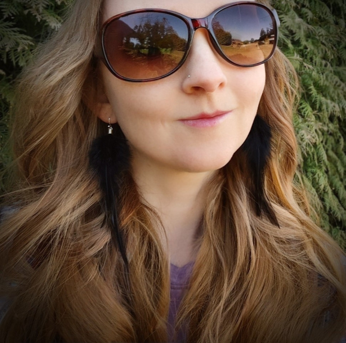 Woman wearing black feather earrings with a green natural background