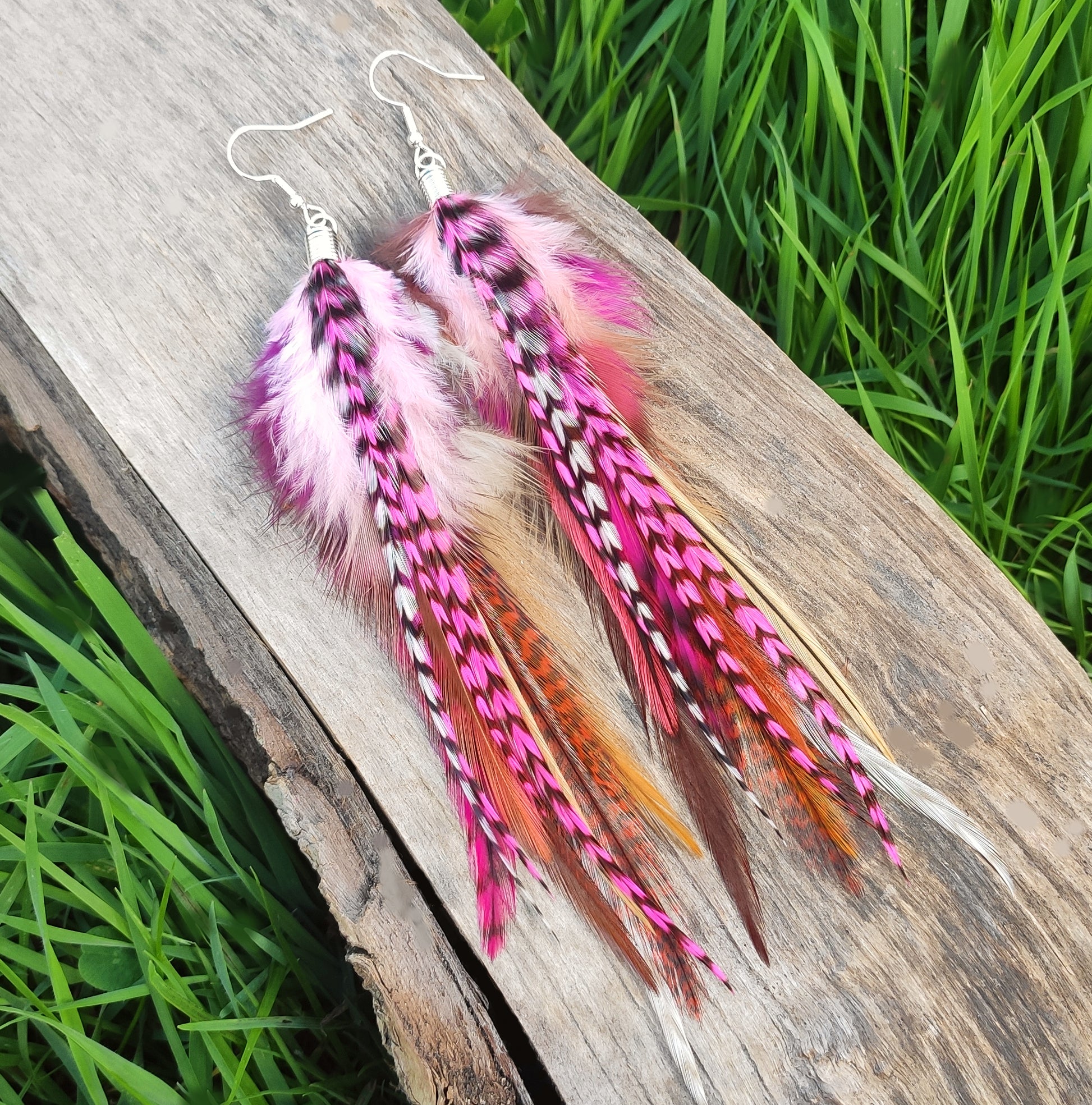 Pink feather earrings on a wooden surface with grass in the background