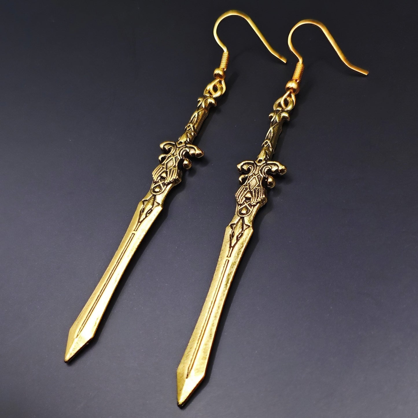 Lightweight long sword earrings made of stainless steel, ideal for medieval costumes. Gold swords on a black background.