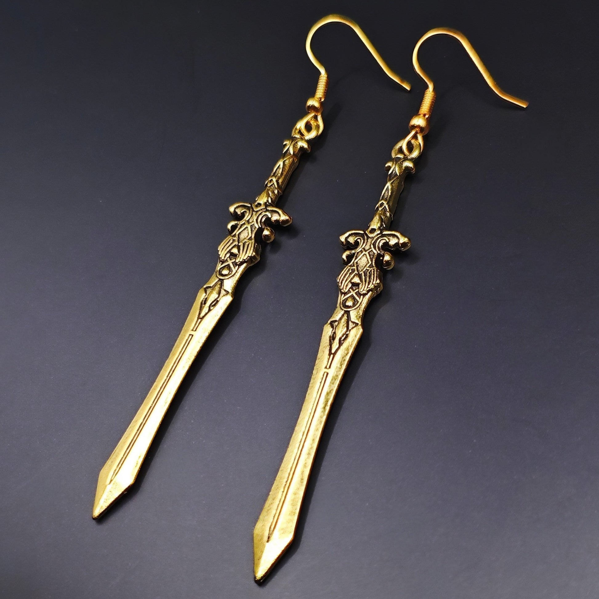 Lightweight long sword earrings made of stainless steel, ideal for medieval costumes. Gold swords on a black background.