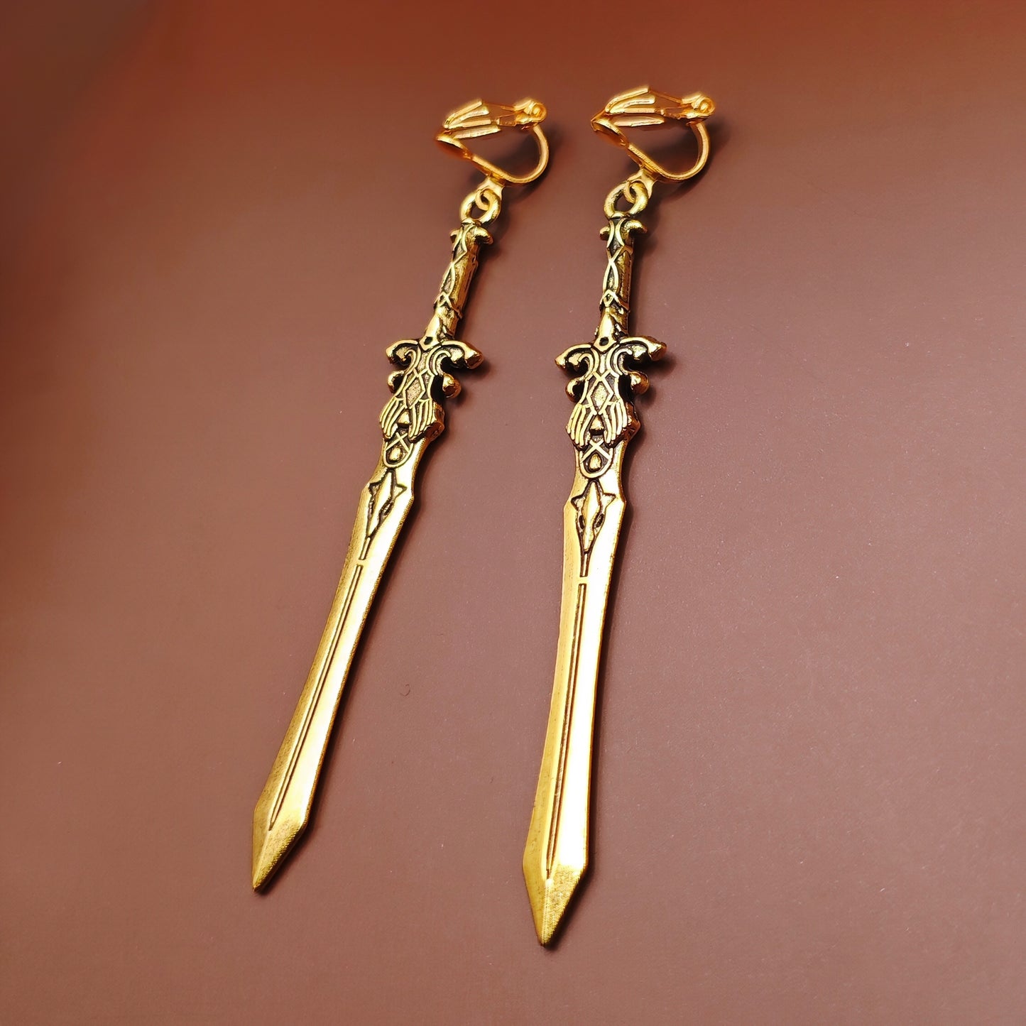 Long gold sword earrings with stainless steel clip-ons. The swords have a fantasy medieval style and look like historical renaissance weapons.