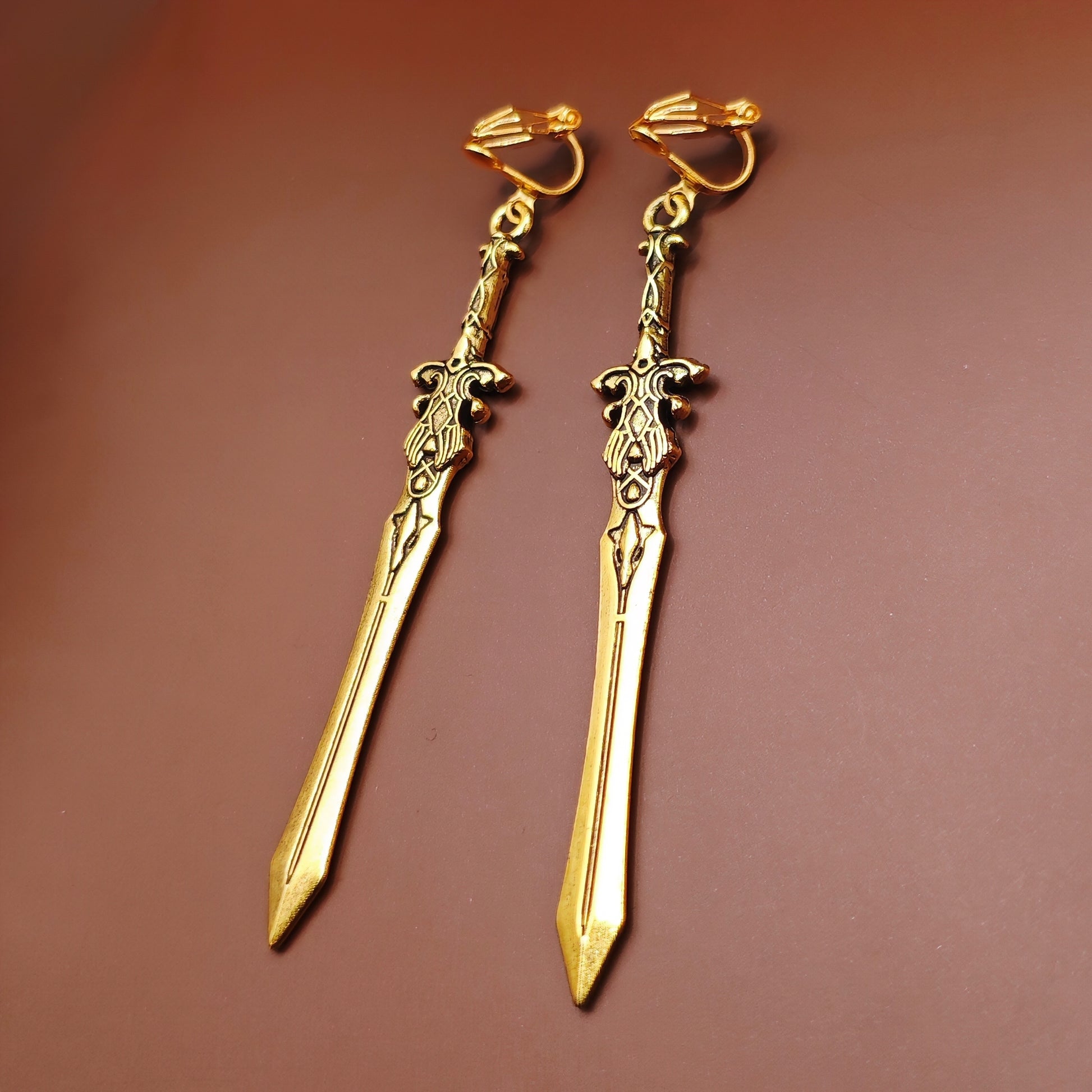 Long gold sword earrings with stainless steel clip-ons. The swords have a fantasy medieval style and look like historical renaissance weapons.