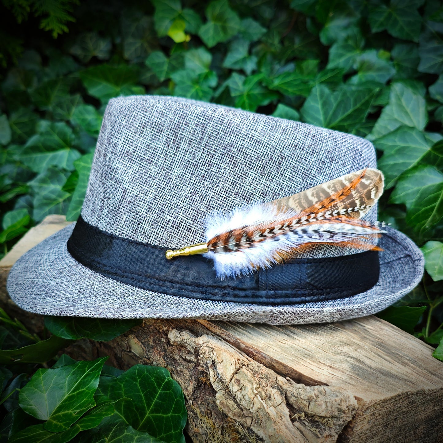 Gray fedora hat with a rustic and boho stripy feather hat pin with green foliage in the background
