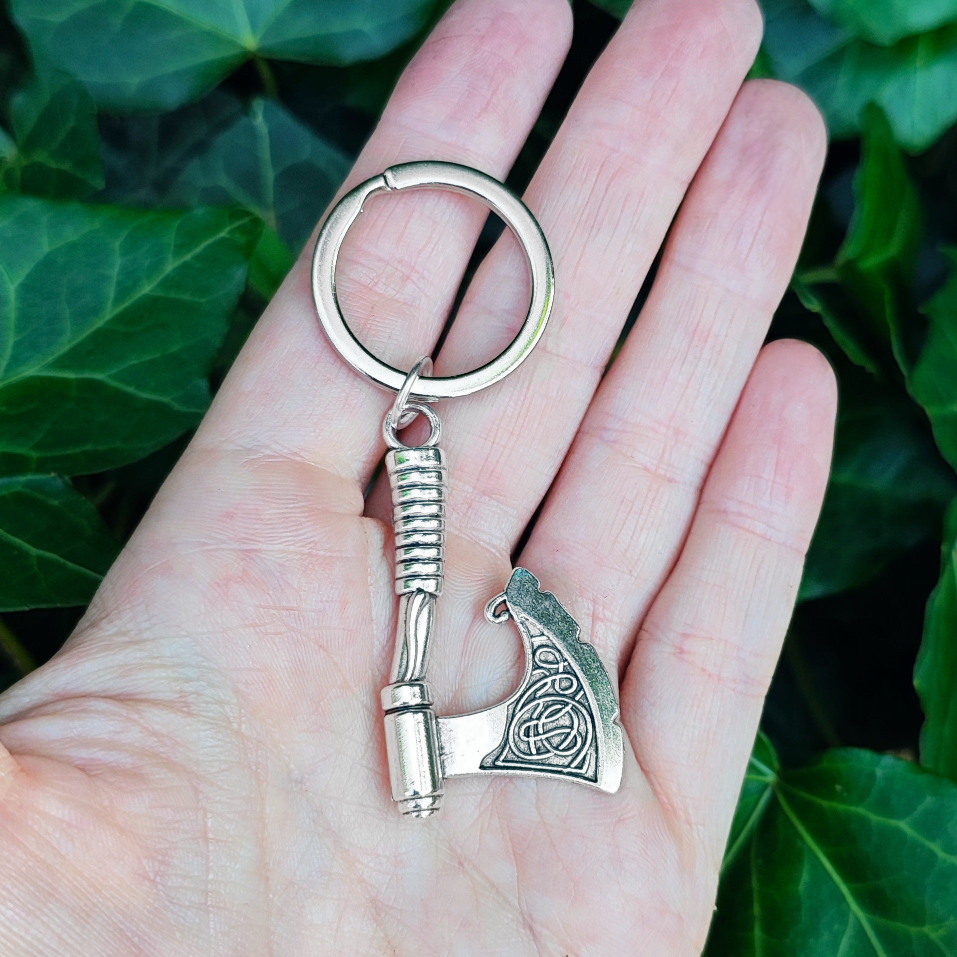 Silver medieval axe keychain held in a hand against a green leafy background