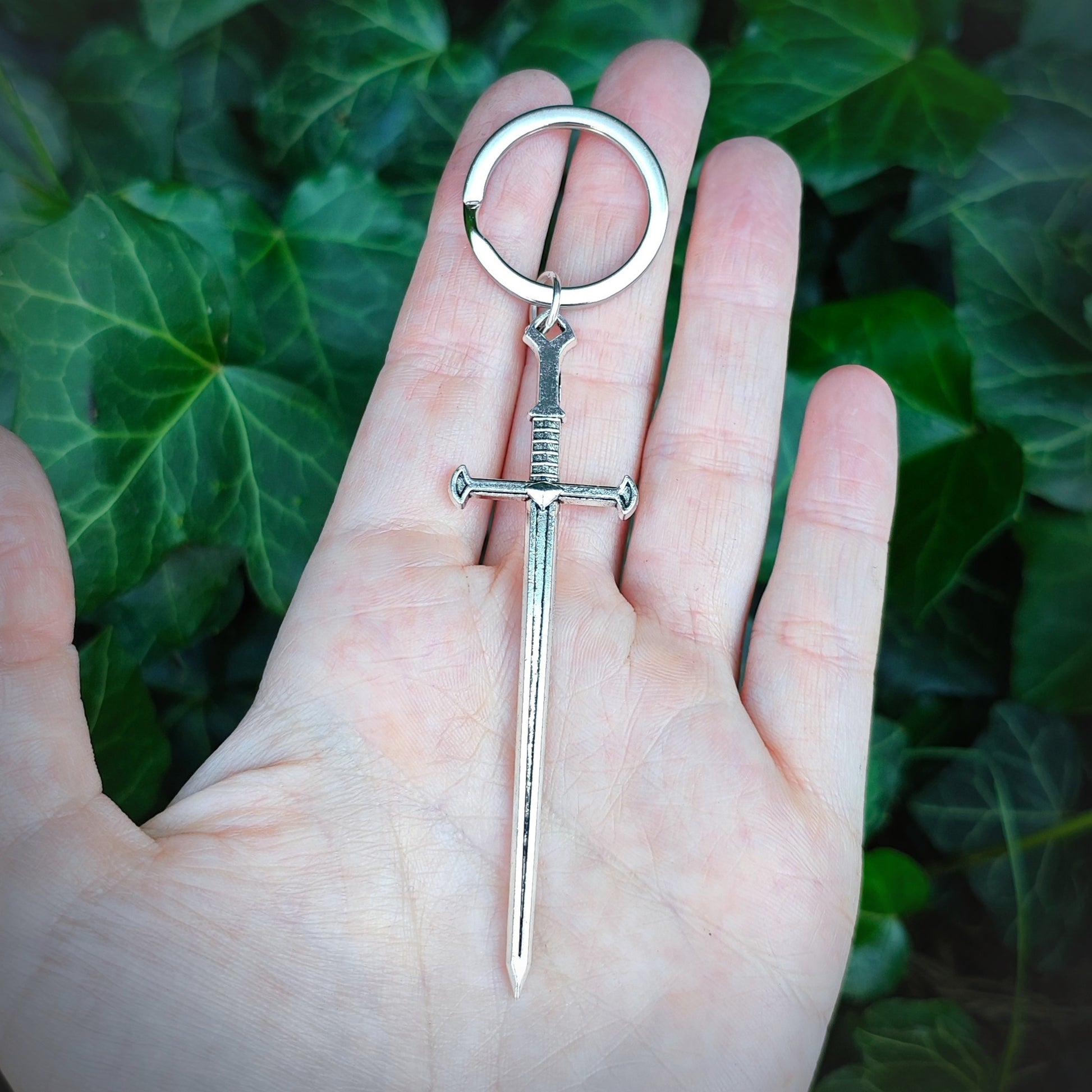 Silver sword keychain held in a hand with a green leafy background