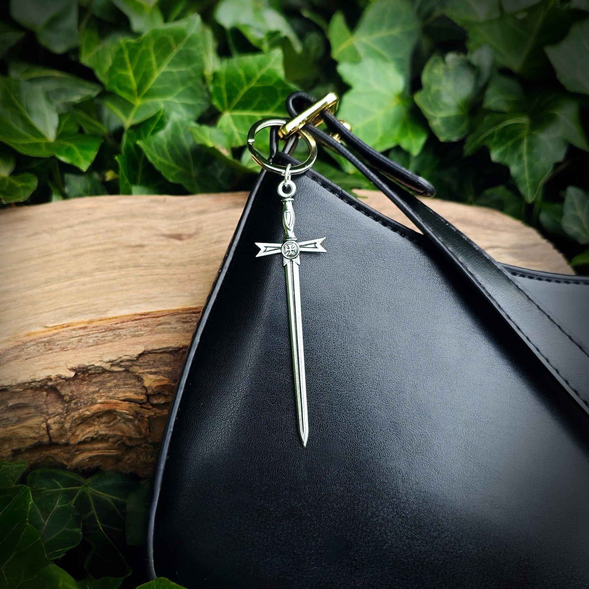 Silver keychain with a sword design attached to a black bag against a green leafy background