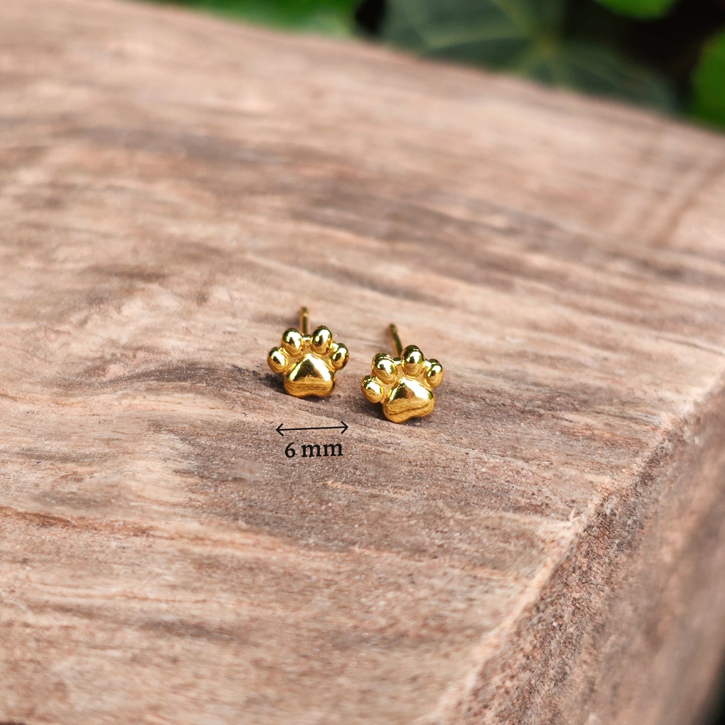 Gold paw print earrings on a wooden surface with a measurement label.
