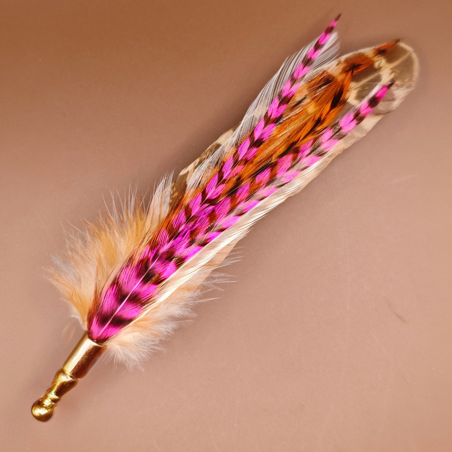 A stripy bright pink, orange, white and beige feather hat pin with gold pin.