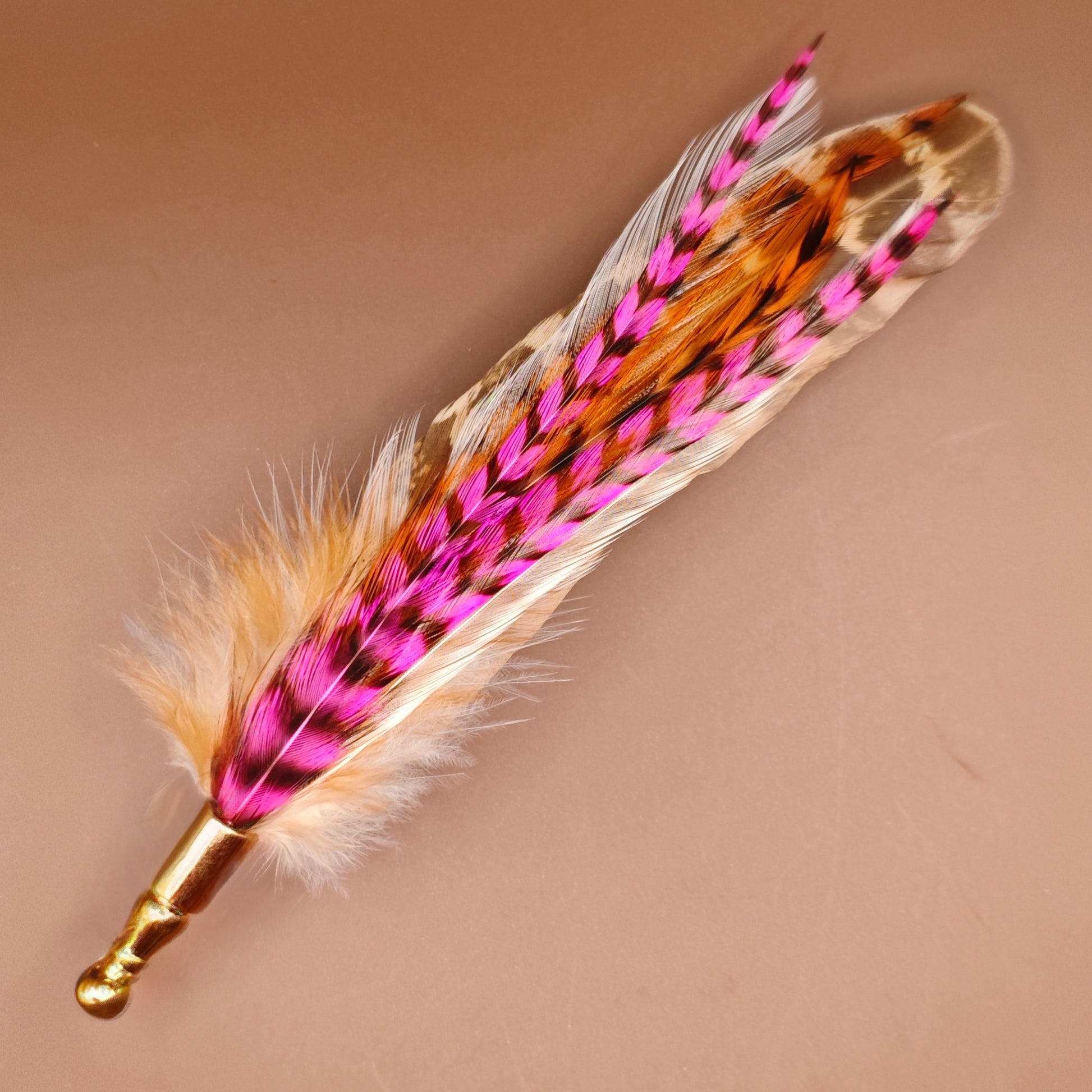 A stripy bright pink, orange, white and beige feather hat pin with gold pin.