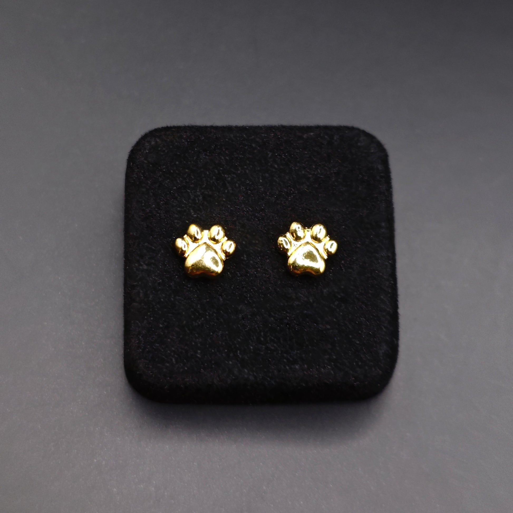 Gold paw print earrings on a black square pad against a gray background