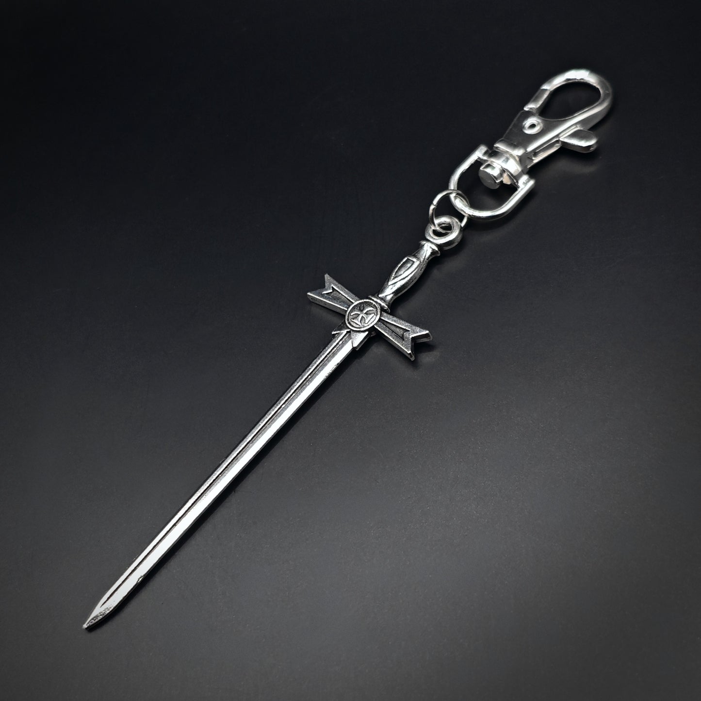 Silver sword keyring with a cross design on a black background