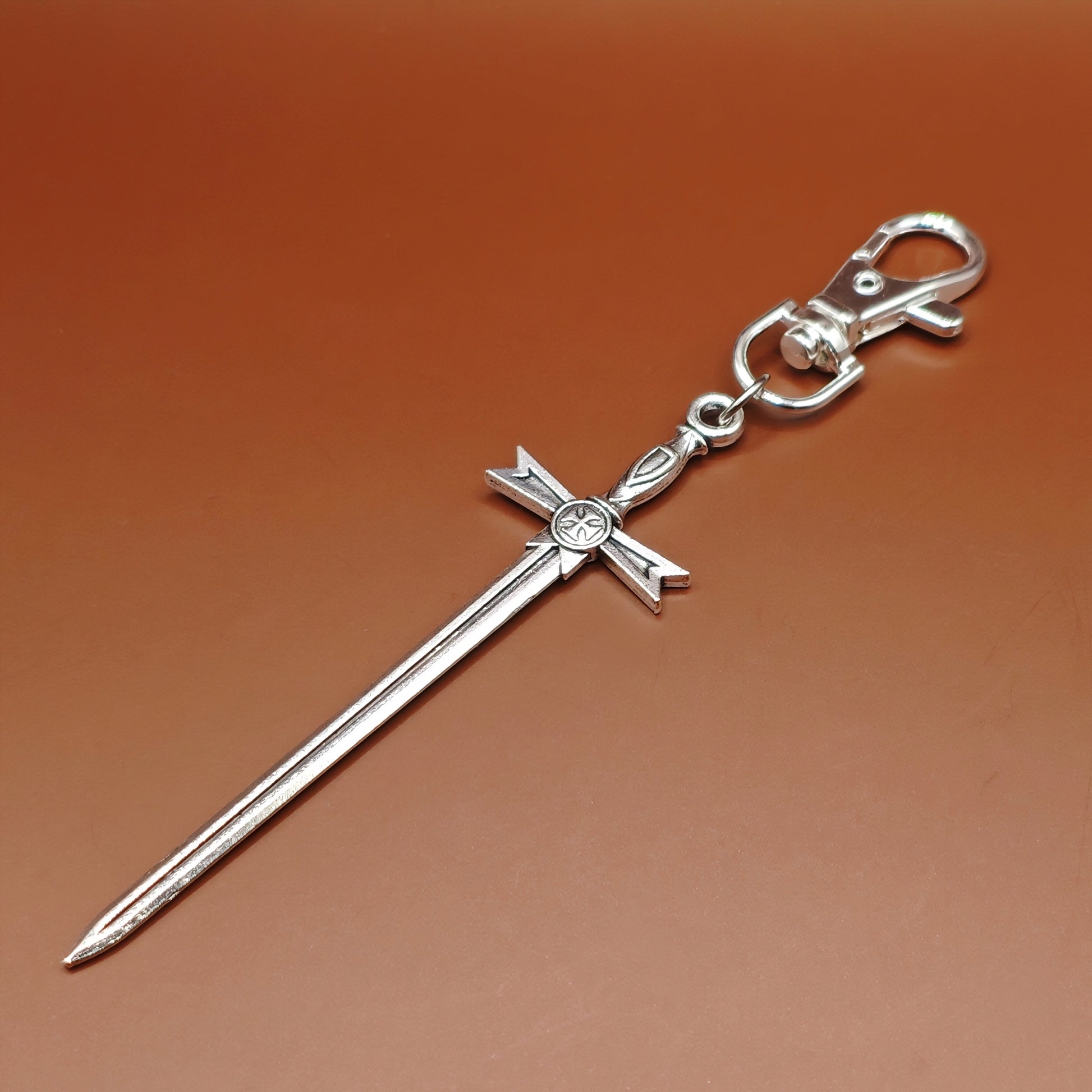 Silver sword keychain with lobster clasp on a brown background. Fantasy medieval style.
