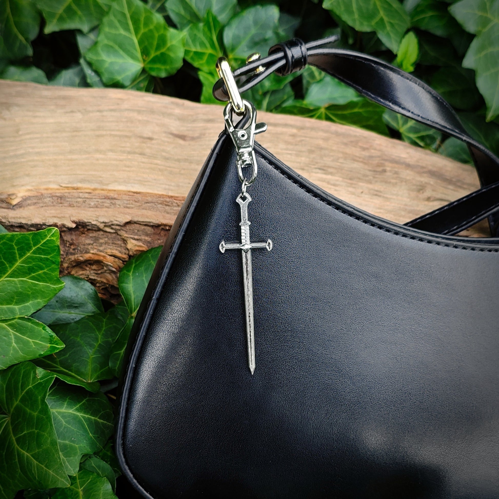 Black handbag with a silver sword bag charm against a natural background