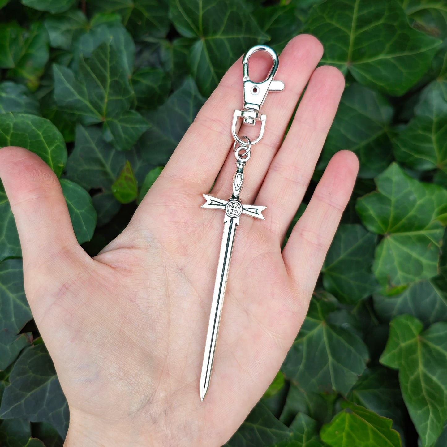 Silver sword keychain held in a hand with a green leafy background