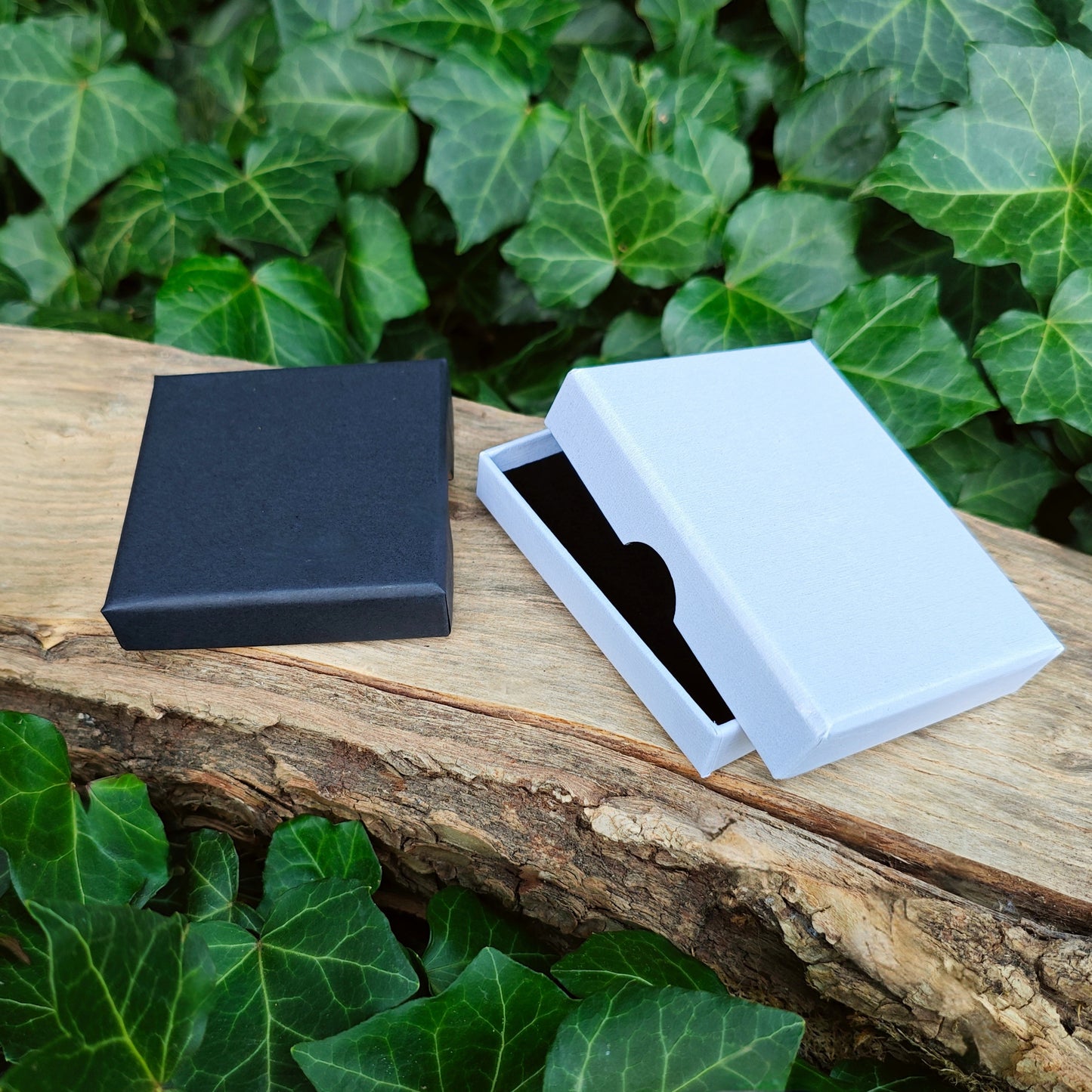 Black and white jewelry boxes on a wooden surface with green leaves in the background
