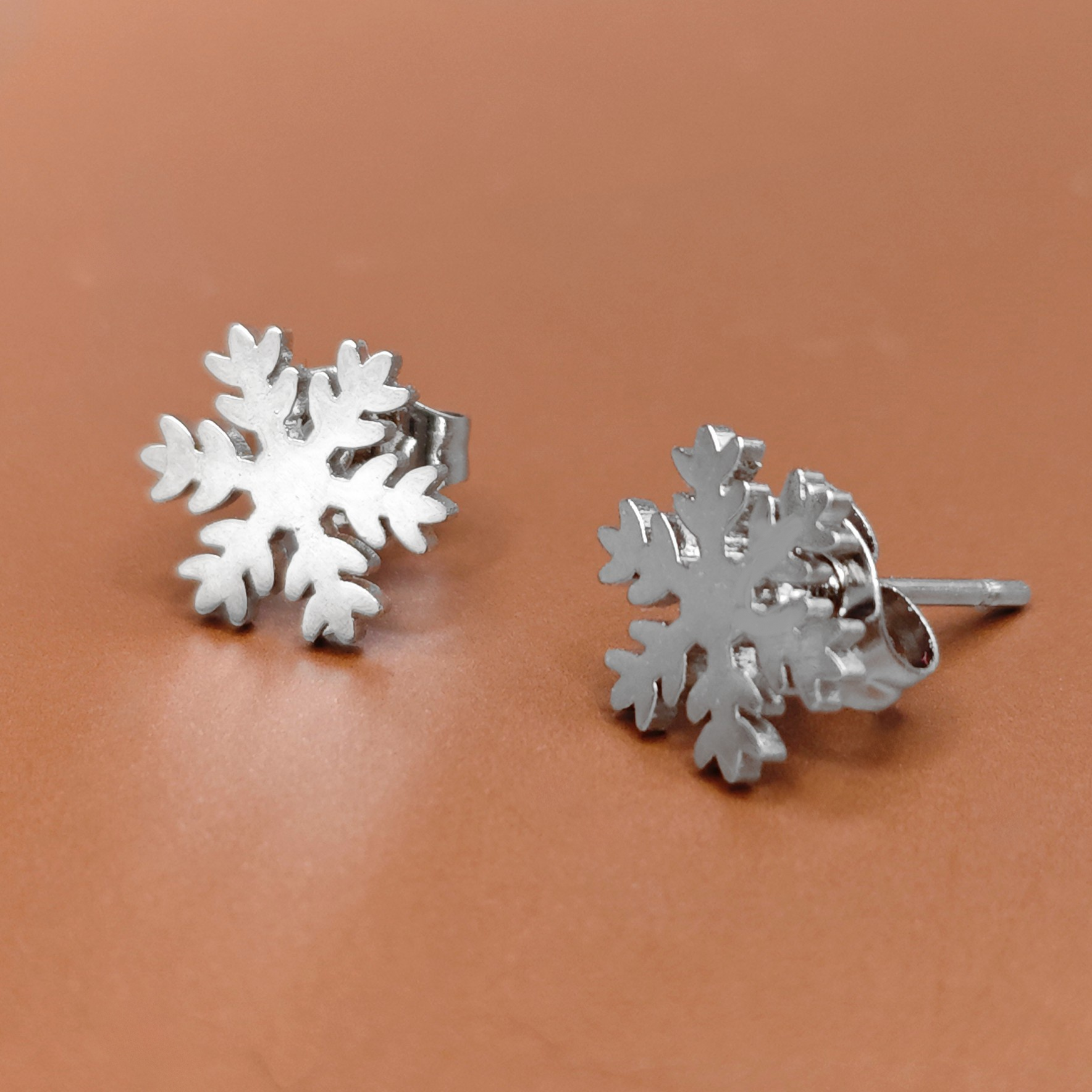 Silver snowflake earrings made with stainless steel on a brown background