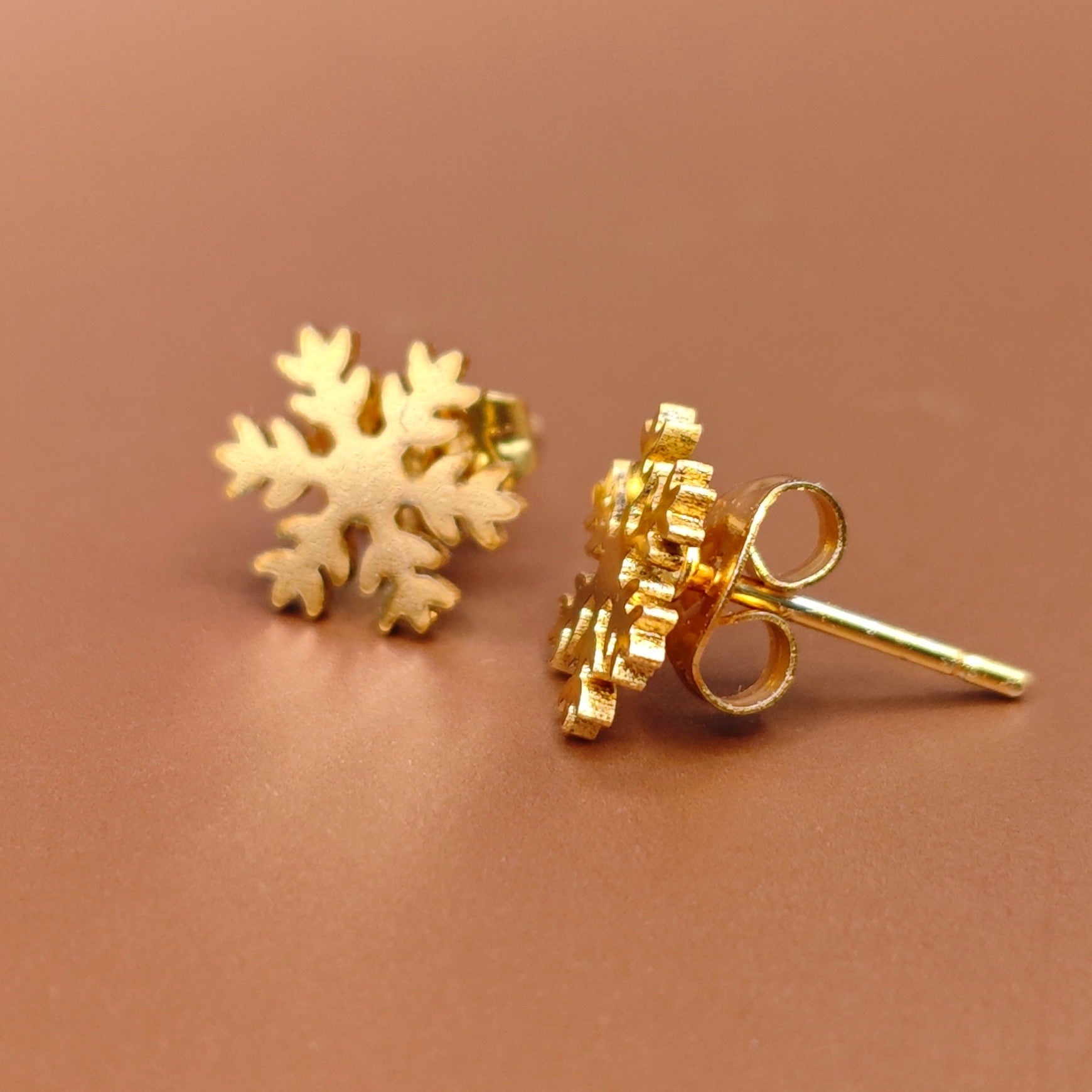 Gold snowflake stud earrings on a brown background. Small gift idea for girls in the holiday season.