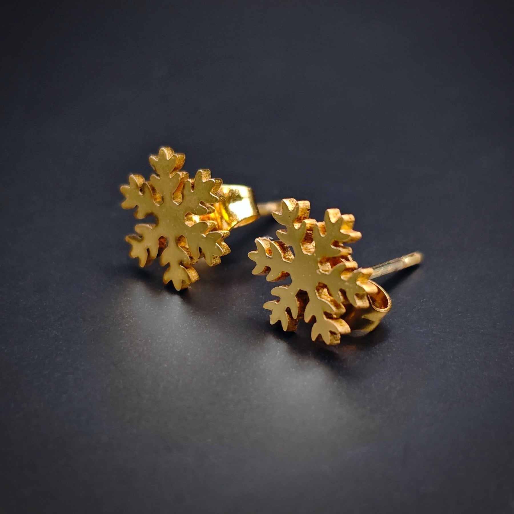 Gold snowflake stud earrings made from stainless steel on a dark background