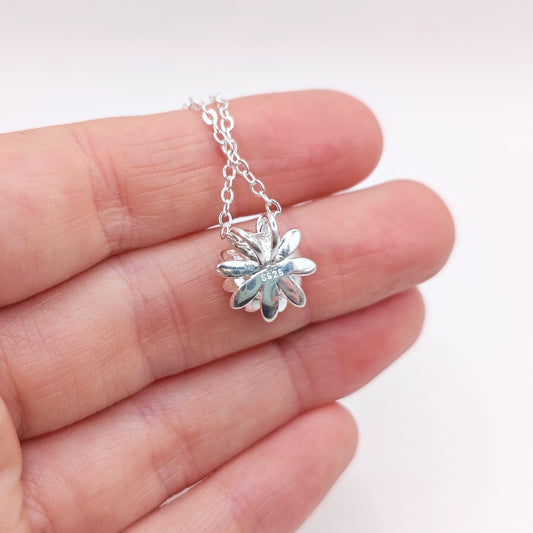 The back of a silver necklace with a flower pendant showing the S925 stamp, held between fingers on a white background
