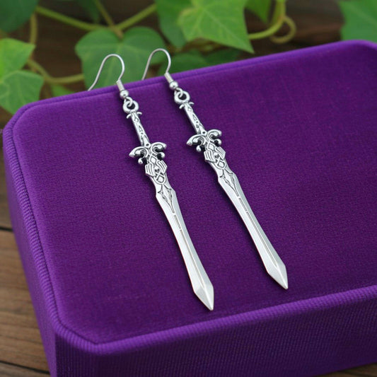 Silver sword earrings on a purple surface with green leaves in the background
