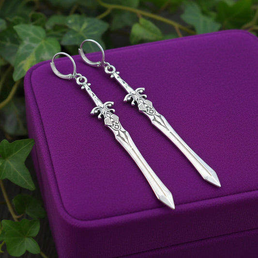 Medieval silver sword earrings with hoops on a purple cushion with green leaves in the background
