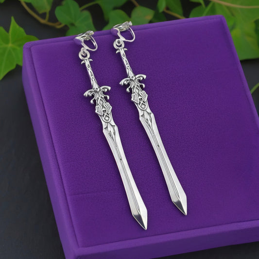 Silver fantasy sword earrings with clip ons on a purple cushion with green leaves in the background