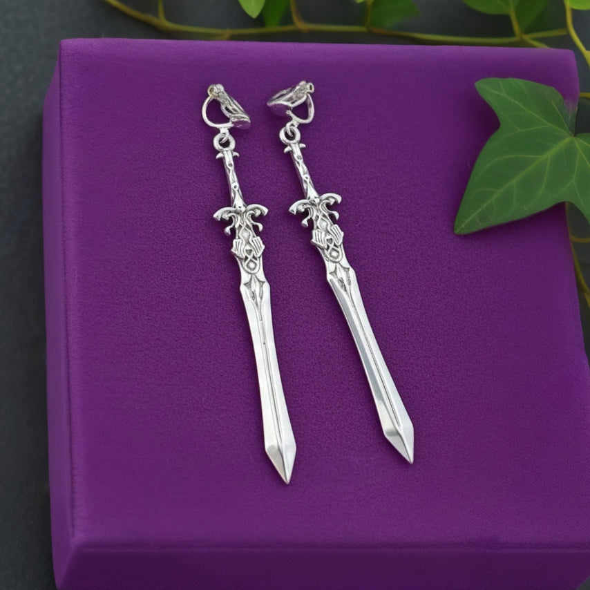 Silver sword-shaped earrings on a purple box with green leaves in the background