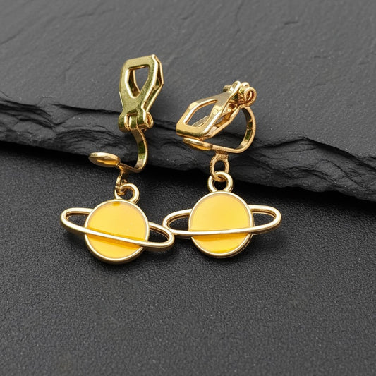 Yellow Saturn planet earrings with gold clip-ons on a black background
