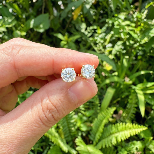 A hand holding sparkly gold 925 silver stud earrings with white cubic zirconia crystals outside in the sun