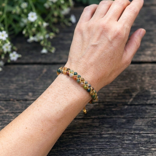 A woman's hand wearing a colourful bead bracelet on a wooden surface with white flowers in the background