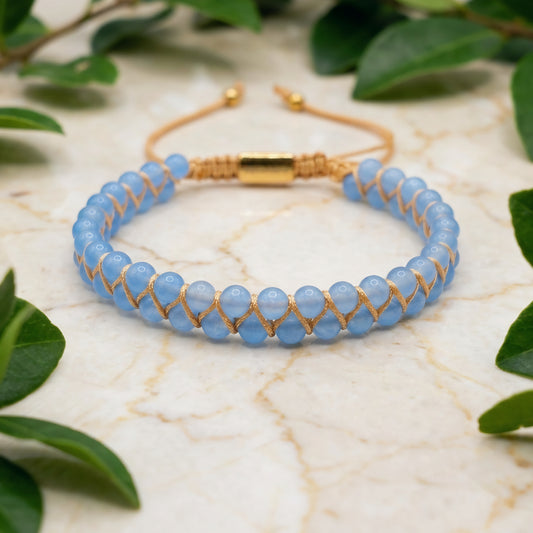 Blue aquamarine beaded gemstone bracelet with gold accents on a marble surface with green leaves.