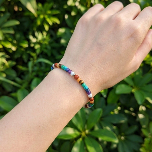 A multicolor beaded bracelet worn on a person's wrist, photographed outdoors against a blurred background of green foliage.