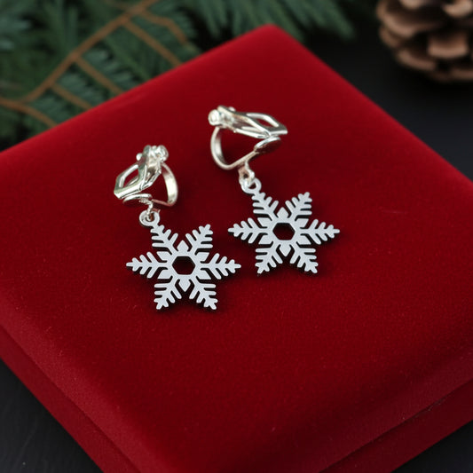 Clip on silver snowflake earrings on a red velvet surface with greenery in the background