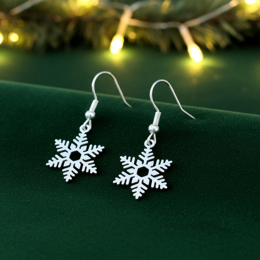 Silver snowflake earrings on a green surface with blurred lights in the background