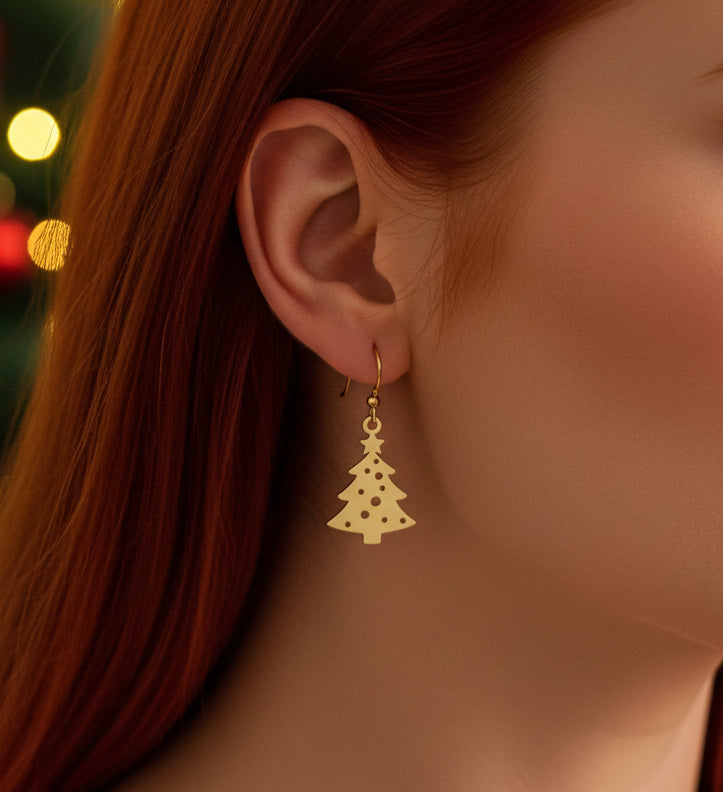 Woman wearing Christmas tree earrings with hooks made from gold stainless steel with lights in the background.