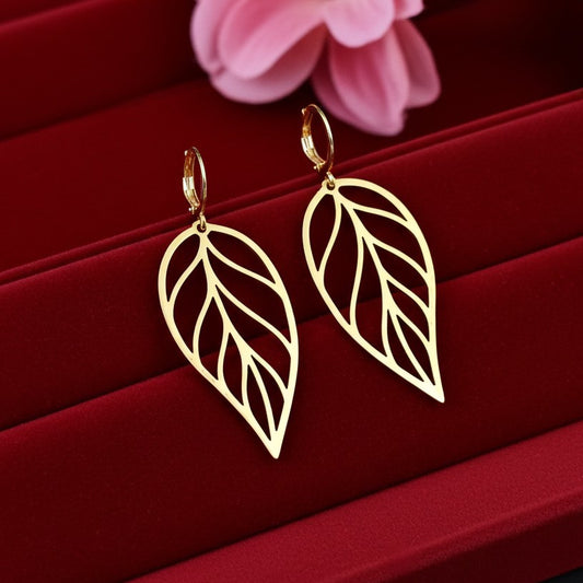 Large gold stainless steel leaf earrings with hoops on a red background