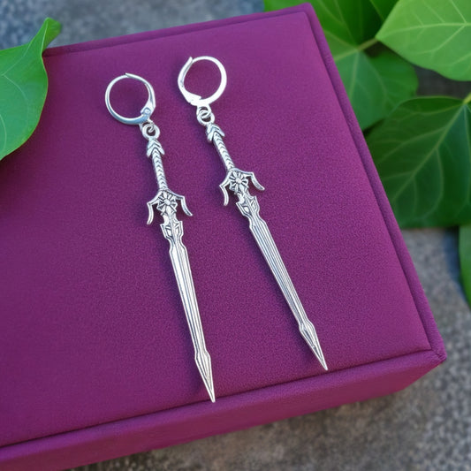 Pair of silver sword earrings with hoops on a purple box