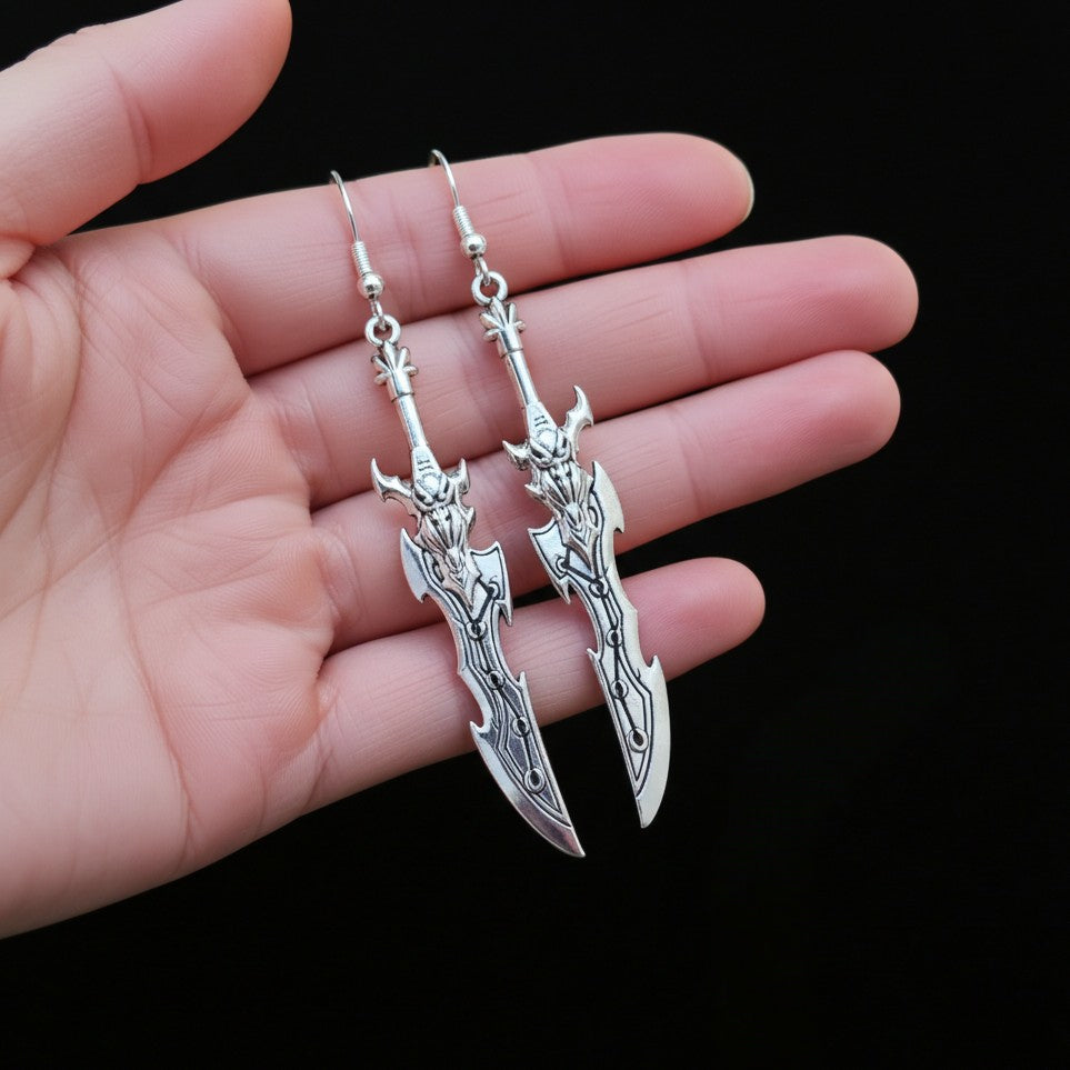 A hand holding silver sword earrings with hooks on a black background