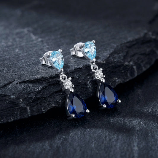 Pair of real silver stud drop earrings with blue gemstones on a dark stone surface