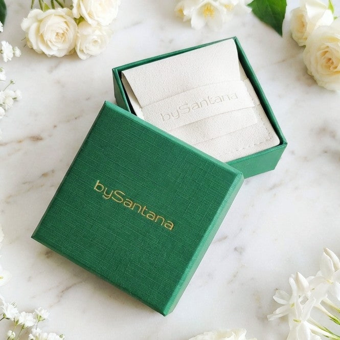 Green jewelry box with 'bySantana' branding on a marble surface with white flowers.