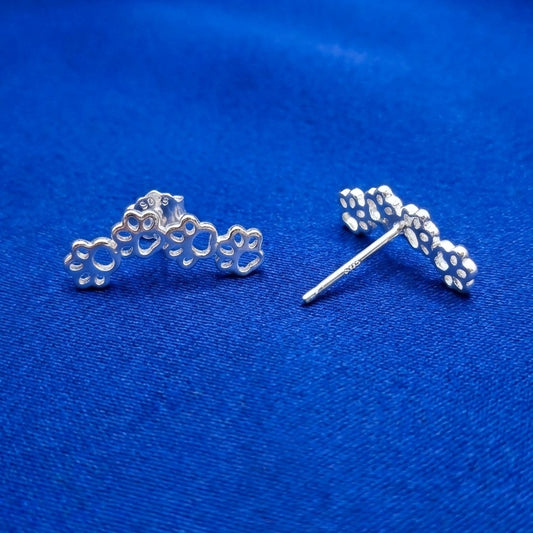 Silver paw print earrings on a blue background. the earrings have 925 on them