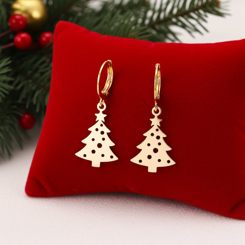 Festive Christmas tree earrings with hoops made from gold stainless steel on red velvet with lights in the background.