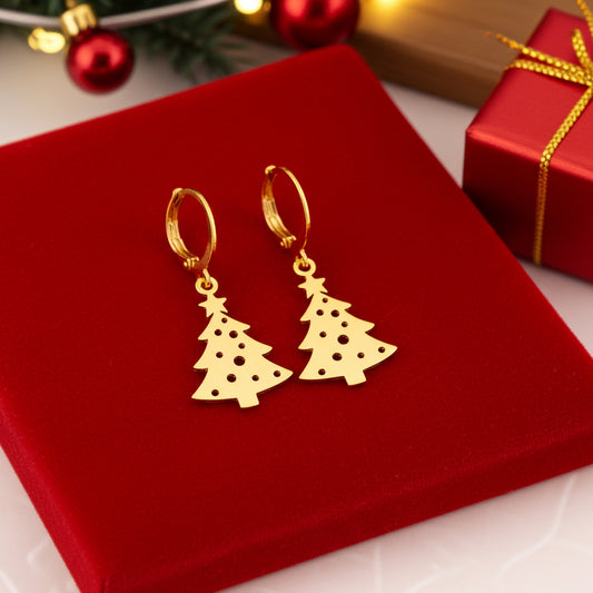 Festive Christmas tree earrings with hoops made from gold stainless steel on red velvet with lights in the background.