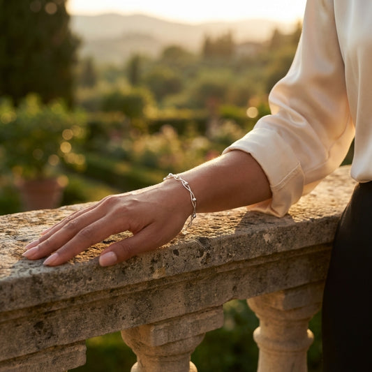 An elegant woman wearings a 925 Silver Bracelet with two intertwined snake chains and round beads. She is outside in an old Italian garden at sunset.
