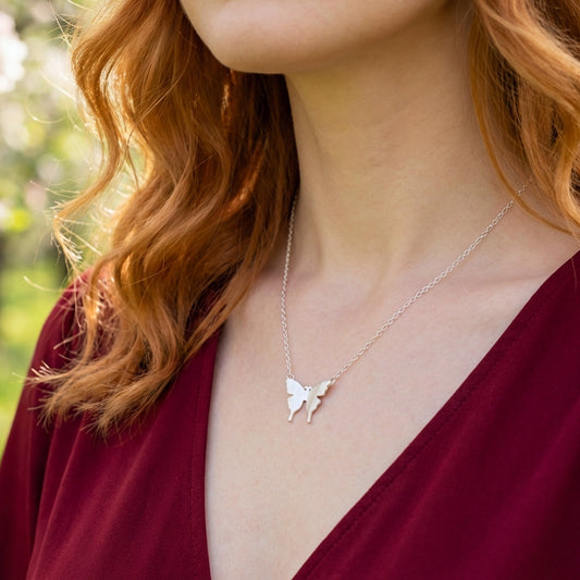 Woman wearing a silver butterfly necklace with blurred greenery in the background