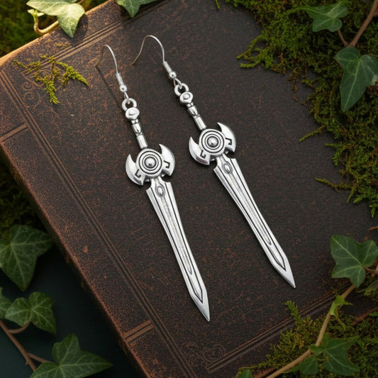 Silver sword earrings on an old book with green leaves